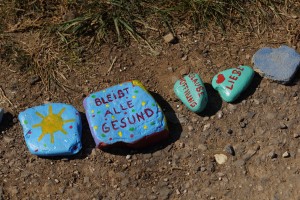 Mehrere Steine, einer ist mit einer Sonne bemalt, andere zeigen Botschaften wie „Glaube, Liebe, Hoffnung“