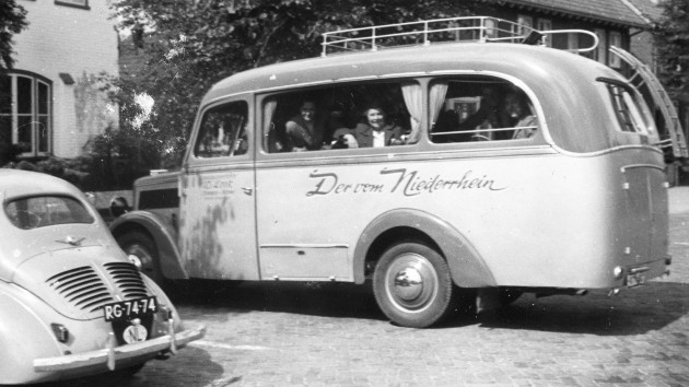 Ein Bus der Firma Look („Der vom Niederrhein“) parkt vor einem Haus, einige Passagiere schauen hinaus; im Vordergrund steht ein Auto mit niederländischem Kennzeichen (Anfang der 1950er Jahre).