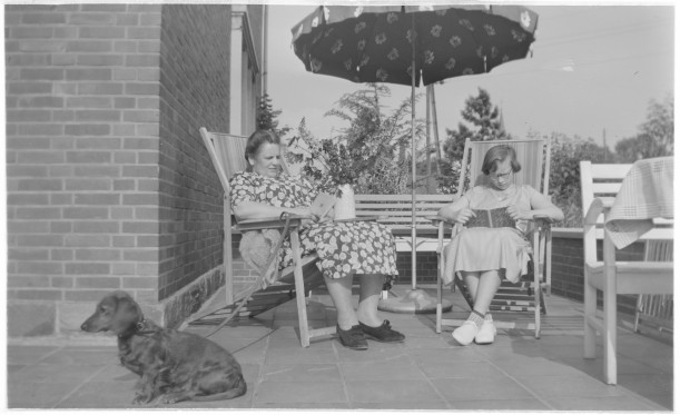 Zwei Frauen sitzen in Liegestühlen auf einer Terrasse und lesen ein Buch.