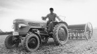 Ein Mann sitzt auf einem alten Fendt-Traktor, der auf einem Feld steht. Das Bild ist scharz-weiß.