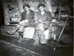 Zwei Bergmänner sitzen rauchend auf einer Kiste und blicken in die Kamera