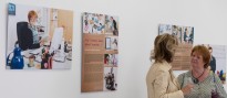 Ausstellungsansichten "Bürowelten" mit einem Rollup im Vordergrund, das Porträts unterschiedlicher Menschen und Objekte zeigt . Im Hintergrund an großen weißen Wandflächen weitere Ausstellungsmotive