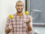 Ein Mann sitzt auf einer Fensterbank und jongliert mit drei Zitronen.