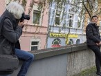 Ein Mann fotografiert einen anderen, der auf einer Mauer sitzt.