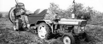 Auf einem Feld fährt ein von einem Mann angetriebener Traktor mit einem größeren Maschine als Anhänger – ein Sammelroder.