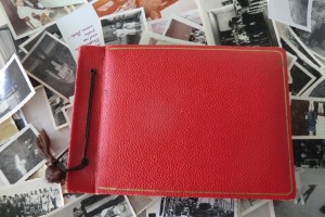 Fotoalbum mit rotem Ledereinband liegt auf zahlreichen, verstreuten schwarz-weiß-Fotografien