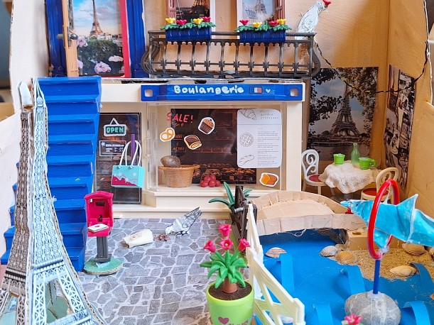 Foto einer dreidimensionalen Collage die einen französisch anmutenden Hauseingang mit Bistrotisch, Liebesbrief, Eiffelturmdeko und vielen weiteren Details zeigt.