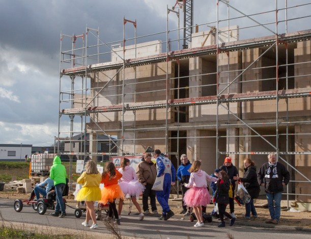 Eine Gruppe bunt kostümierter Menschen zieht durch ein Neubaugebiet. Im Hintergrund der Rohbau eines großen Hauses.