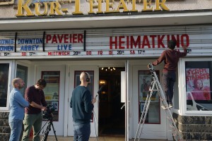 Foto: Ein Kamerateam filmt einen Mitarbeiter eines Kinos, welcher Buchstaben vor einem Kino aufhängt.