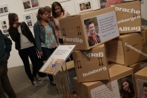 Schulklasse beim Ausstellungsbesuch: Installation von Umzugskartons mit Porträts und Zitaten