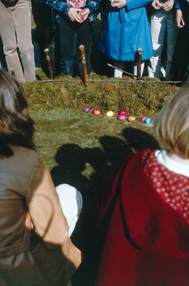 Kinder sitzen auf einer Rasenfläche und spielen mit bunten Ostereiern.