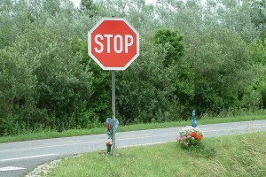 Stoppschild an einer Straßenkreuzung, darunter erinnern Blumen an einen Unfall.