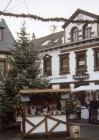 Ein kleiner Weihnachtsmarkt vor einer historischen Kulisse. Vor einer Häuserwand, hinter einem einfachen Stand, steht ein großer Weihnachtsbaum.