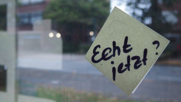 Ein Post-it klebt auf einem Fenster. Auf ihm steht mit dickem Stift geschrieben: "Echt jetzt?" Im hintergrund ist eine verschwommene Straße.