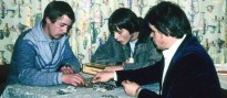 Drei junge Männer sitzen an einem Tisch und zählen Geld, vor allem Münzen
