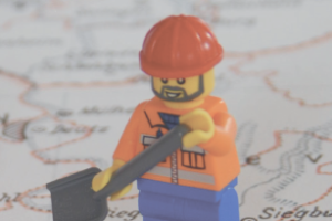 Lego-Bauarbeiter-Männchen auf Stadtkerte im Hintergrund, im Vordergrund Titel der Tagung: Erfinden, Empfinden, Auffinden