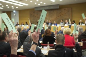 Auf dem Foto sieht Menschen, die mit erhobenen Händen eine Abstimmung durchführen.