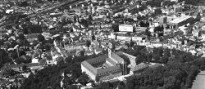 Luftaufnahme in schwarz-weiß. Im Vordergund der Michelsberg mit Kloster und Wald., dahinter der Ortskern.