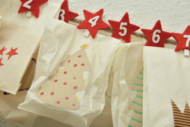 Brottüten, die mit Weihnachtsbäumen bemalt sind und an einer Schnur mithilfe von Sternklammern, auf denen die Zahlen zwei bis sieben notiert sind, befestigt sind