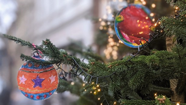 Detail eines Weihnachtsbaums in einem Straßenzug, am Tannenzweig zwei bunte Papieranhänger in Form von Weihnachtskugeln und eine Lichterkette