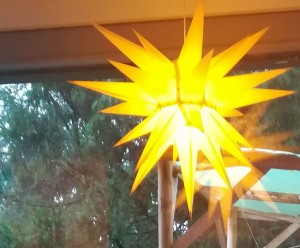 Beleuchteter gelber Deko-Stern vor einem Terassenfenster mit Aussicht ins Grüne