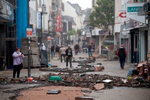 Die zerstörte Euskirchener Innenstadt mit kaputten Läden und aufgerissenen Straßen. Leute laufen ungläubig umher.