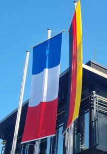 Vor einem Gebäude sind die blau-weiß-rote Frankreichflagge und die schwarz-rot-goldene Deutschlandflagge gehisst.