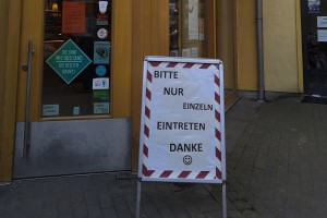 Plakataufsteller vor dem Eingang zu einer Bäckerei, Aufschrift: Bitte nur einzeln eintreten Danke.