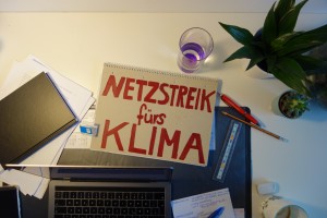 Schreibtischausicht mit PC mit Schild "Netzstreik fürs Klim"