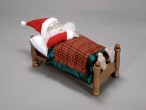 Ein Weihnachtsmann in Puppengröße liegt in einem Bett und schläft.