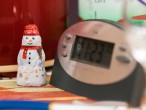 Auf einen Tischchen befinden sich eine Digitaluhr, ein Rezeptblock, Stifte, ein Stifthalter, Thermoskanne, Wasserflasche und ein Trinkglas. Dazwischen steht ein kleiner Schokoladen-Schneemann. 