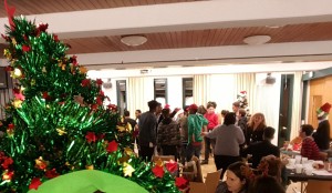 Im Vordergrund grüne, glitzernde Weihnachtsdeko, im Hintergrund tanzen und unterhalten sich junge Leute.