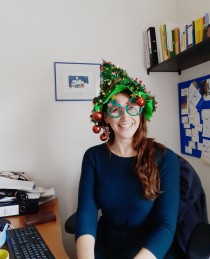 Frau mit glitzerndem Weihnachtshut und Weihnachtsbrille am Schreibtisch.