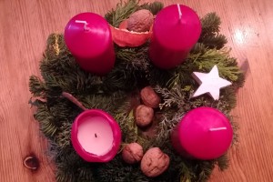 Adventskranz mit vier dicken, roten Kerzen, eine davon hat einen bereits angebrannten Docht