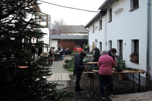 Im Innenhof eines Schweinheimers werden an verschiedenen Tischen fleißig Adventskränze gebastelt. Tannengrün, Dekorationsmaterial und anderes Equipment ist zu sehen.