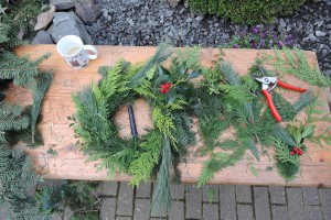 Auf einem Tisch liegt ein frisch gebundener Adventskranz, noch ohne Dekoration, daneben eine Schere und überschüssiges Tannengrün.