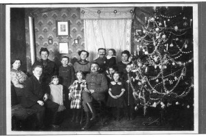 Festlich gekleidete Menschen stehen um einen geschmückten Weihnachtsbaum.
