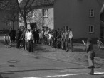 Ein Mann steht vor einer auf eine Straße gemalten weißen Linie in Wurfhaltung. Im Hintergrund stehen zahlreiche zuschauende Personen.