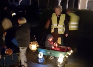 Eine Gruppe von Kindern und Erwachsenen steht mit Laternen vor einem Hauseingang.