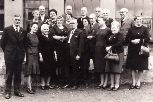 Ehemalige Schülerinnen und Schüler posieren mit ihrer Lehrerin vor einem Gebäude für das Foto.