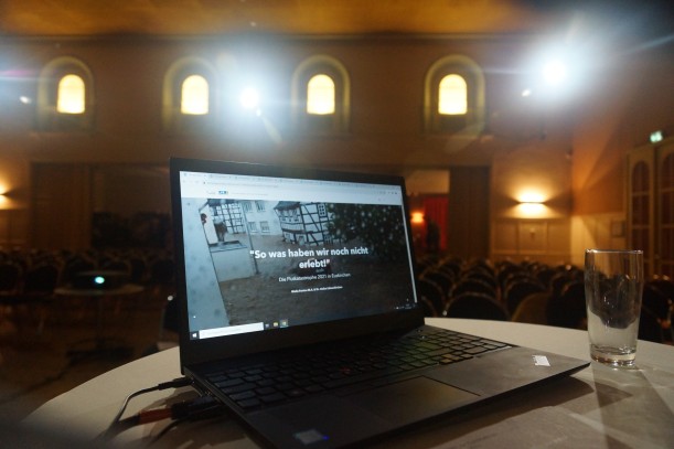 Ein Laptop in einem schön beleuchteten Saal, auf dem die Startseite der digitalen Ausstellung geöffnet ist.