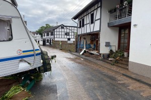 Die zerstörte Schweinheimer Straße mit Schlamm, querstehendem Wohnmobil und einem Haus mit zerstörter Front.