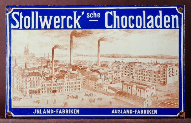 Emaille-Tafel mit dem Schriftzug „Stollwerck’sche Chocoladen, Inland-Fabriken, Ausland-Fabriken, Abbildung einer Fabrik im Vordergrund, im Hintergrund der Dom.