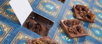 Blaue Pappschachtel mit goldfarbiger islamischer Ornamentik und Zahlen auf den Ausklapptürchen. Ein paar Türchen sind geöffnet und lassen Schokoladenstücke mit Datteln erkennen.