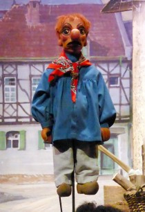 Stockpuppe aus Holz mit blauem Hemd, rotem Halstuch und prägnanter Knollennase.
