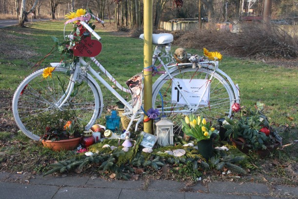 Ein weißes Fahrrad mit Pflanzen/Blumen geschmückt steht an der Stelle, an der ein Radfahrer im Straßenverkehr gestorben ist. Es ist Teil einer privaten Trauer-, Mahn- und Gedenkstätte.