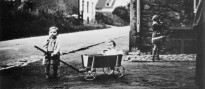 Ein kleiner Junge zieht auf einer unbefestigten Straße einen Bollerwagen, in welchem ein Kleinkind sitzt.