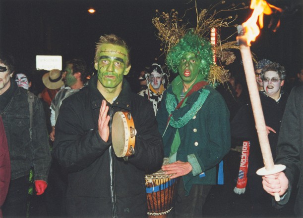 Schaurig kostümierte Männer machen mit dem Tamburin und Bongo Musik. Von rechts ragen Pechfackeln ins Bild.