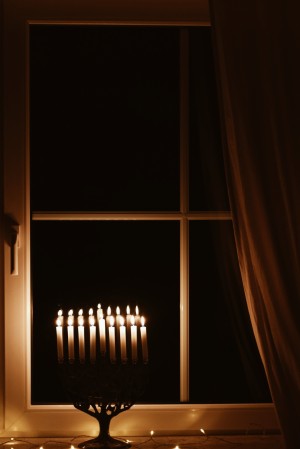 Auf der Fensterbank steht die Channukia, ein achtflammiger Leuchter mit einer versetzten neunten Lichtquelle. Alle Kerzen brennen und erhellen die Dunkelheit.